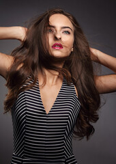 Makeup mystic indian woman with long hair, pink lipstick with wind hair in striped dress on grey background. Closeup