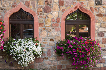 Fototapeta na wymiar View of a stone wall with two windows decorated with flowers 