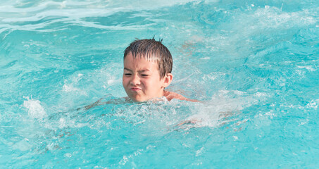 Asian boy is swimming in pool on summer day.