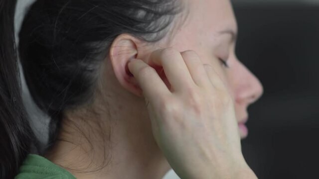 Closeup of young woman putting bluetooth, wireless ear buds, headphones in ear