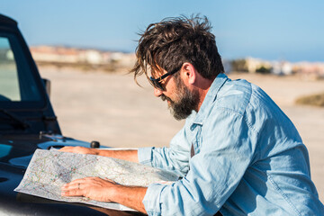 Adventure travel lifestyle - bearded adult man looking paper map to plan the trip and journey - people choosing destination - wanderlust life and car vehicle transport