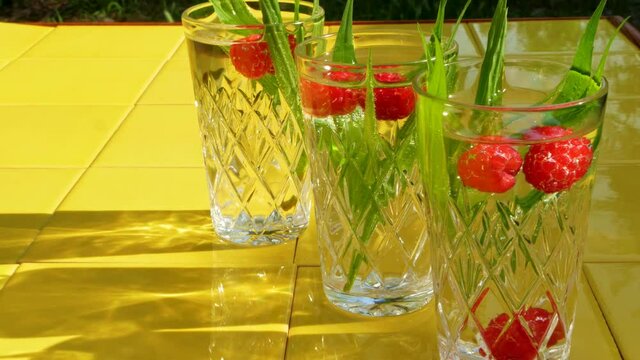 Refreshing summer drinks in crystal glasses with green leaves raspberry yellow tile background shadows. Sweet cold natural cocktail hot summer day. Soda water fruits berries mint tonic. Party vacation