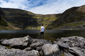 Fototapeta na wymiar 67 / 5000 Resultados de traducción Man standing on stones on the coast of coumshingaun lake Ireland 