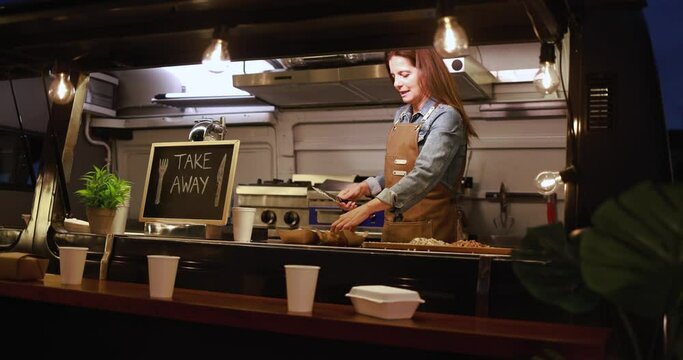 Caucasian chef woman working inside food truck at night time preparing dinner food - Summer and small business concept