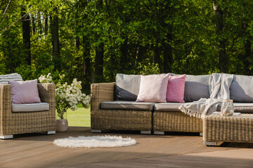 Cozy wooden terrace with grey sofa with pastel pink pillows and blanket