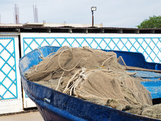 A rolledup fishing net lies in an old blue shabby boat in the bright sun outdoors