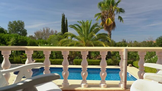 The movement of the video camera from left to right, to the side, stone columns of the terrace, the balcony of the villa, overlooking the beautiful pool. A garden with palm trees for tourists.