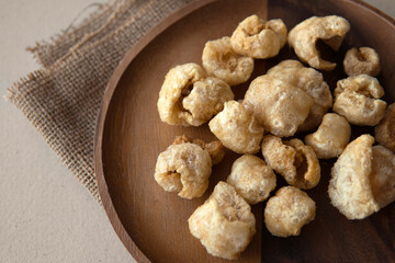 Closeup cooked Pork crackle in dark brown split stained acacia or teak wooden plate on folded hessian or burlap with grey cardboard box recycled paper background