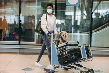 Fototapeta na wymiar Woman traveler in face mask with luggage trolley at airport