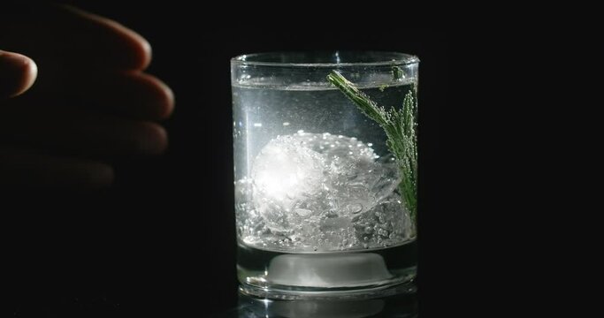 Man's hand touches the glass with cocktail and the glass lights up, cocktail on the black background, cold beverage, refreshment cocktail, 4k Prores HQ 60 fps