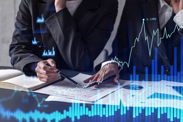Two traders researching historic data to predict stock market behavior. Women in trading business concept. Forex and financial hologram chart over the table with the document.