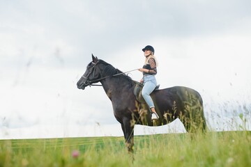 Young woman riding a horse on the green field