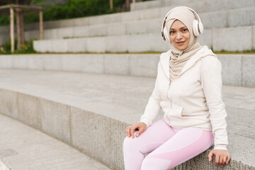 Middle eastern woman in hijab listening music with wireless headphones