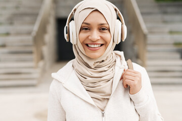 Middle eastern woman in hijab listening music with wireless headphones
