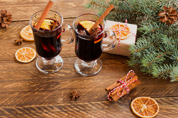 Glasses with Hot red mulled wine for winter and Christmas with orange slice, anise and cinnamon stick decorated with fir branches and wrapped presents for holidays. Festive greeting card