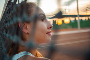 Fototapeta na wymiar Portrait of a beautiful girl. Athlete on the tennis court. Grid, sunset. rest after training. Smiles, happy, sunny glare. Active lifestyle, outdoor. mesh in the foreground