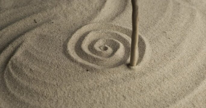 Drawing a spiral in the sand with a wooden stick. Rotation sand in the form of a spiral. Beautiful lighting effects.
