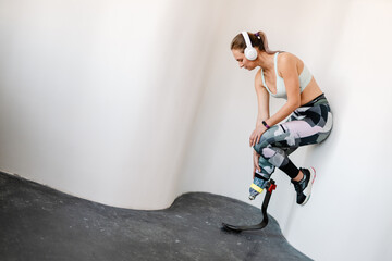 Young sportswoman with prosthesis working out by wall indoors