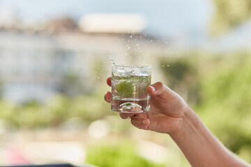 Man holds in his hands a glass of homemade cocktail of hard seltzer with herbs in front of...