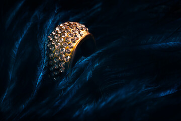 Closeup of luxury wedding ring in dark blue feather background. Bridal golden jewelry gift with...