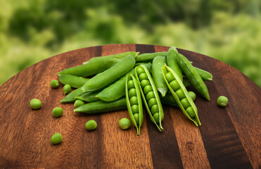 Fresh green peas on a wooden board in front of the natural background.