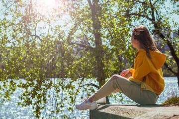 A girl in a yellow sweatshirt  sits on a ledge and enjoying against a blue sky in windy and sunny...