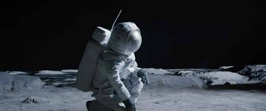 CU Portrait of Caucasian female lunar astronaut finds something and kneels while exploring Moon surface. Shot with 2x anamorphic lens