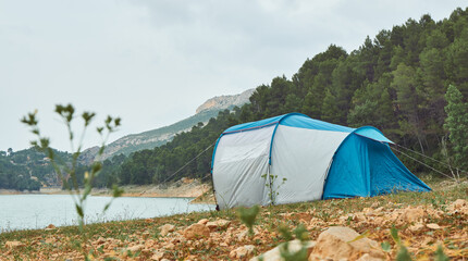 Tent on the shore of a lake with the forest and mountains in the background