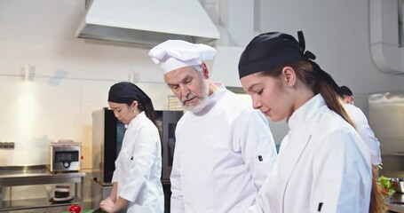 Close up of experienced famous senior Caucasian man chef preparing food at restaurant kitchen and speaking with female cook apprentice teaching to prepare meal. Working process, cookery concept