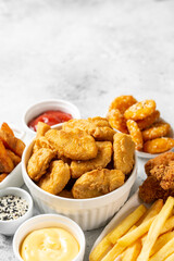 Chicken nuggets, strips, french fries, fried potatoes, ketchup and cheese sauce on a light background. Fast food closeup	