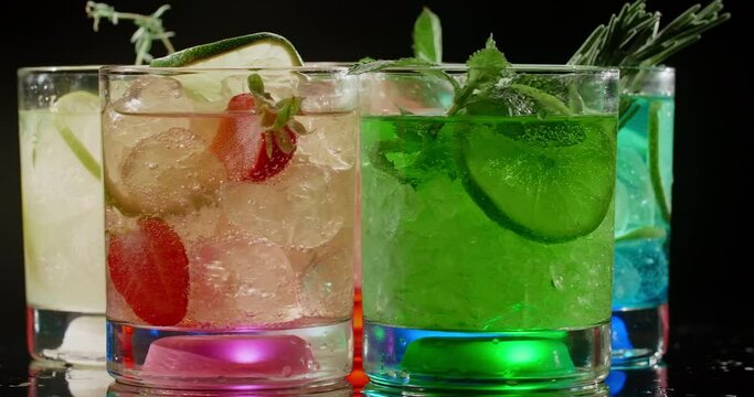 Cold colorfull cocktails are spinning on the black background, lightened glasses, refreshment drinks, 4k Prores HQ