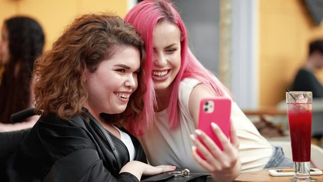 A smiling disabled woman is taking a selfie photo with her friend while sitting on the street cafe outside