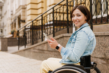 Brunette woman using mobile phone while sitting in wheelchair