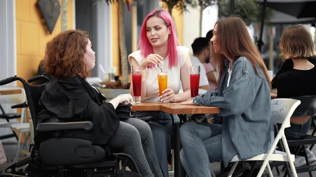 A side view of a pleased disabled woman is talking with her friends while sitting on the street cafe outside
