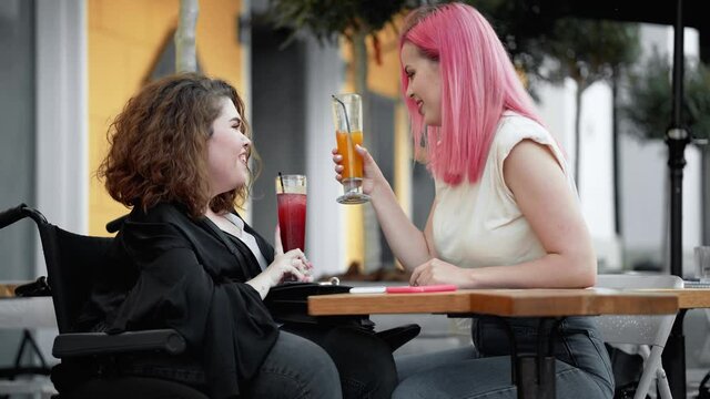 A happy disabled woman is drinking cocktails with her friend sitting on the street cafe outside