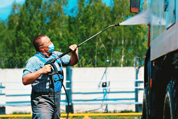 Car wash for special equipment and trucks. A male driver wearing a medical mask washes a truck with...