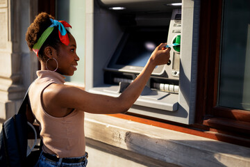 Fototapeta na wymiar Beautiful african women using ATM machine. Attractive young woman withdrawing money from credit card at ATM