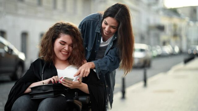 A happy disabled woman is spending time with her friend is walking and using her smartphone on the city street