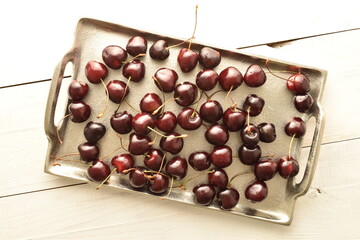 Several ripe organic, dark red cherries with a metal tray on a wooden table, close-up, top view.
