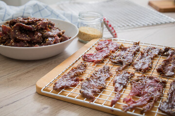 Asia Marinierte Rindfleisch Streifen roh für hausgemachtes Beef Jerky Trockenfleisch mit Sesam und Chili auf Edelstahl Trockengitter für Dörrautomat in Küche mit Holz Brett Hintergrund hell
