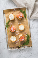 Gravlax Graved Lachs, ein roh gebeizter Fisch mit Dill auf Brötchen mit Frischkäse,  Zwiebelringe auf Backblech mit Backpapier und hell Marmor Hintergrund