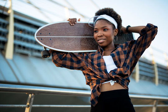 Portrait of happy african-american woman with skateboard. Young stylish woman with skateboard outdoors