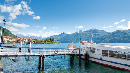 Gangway leading to a ferry-boat at the small harbour of Menaggio, Lake Como, Italy. Italian alps mountain range, with blue sky and clouds on the background.