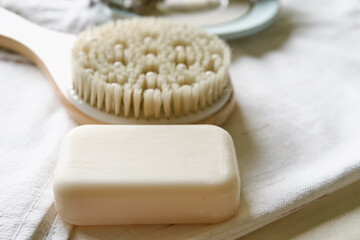 Handmade organic white soap with the body brush close up. Bath accessories on a white towel. Daily body care concept, organic bath products        