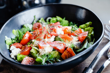 Salad with goat cheese, tomato, iceberg lettuce in big black bowl. Healthy eating, healthy lifestyle concept.