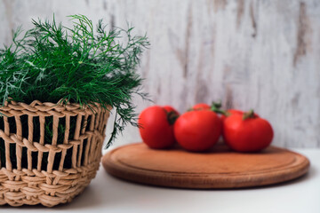 Fresh harvest vegetable background. Green dill in a wicker wooden basket and tomatoes on a big wooden plate. Organic healthy vegan nutrition. Empty space for your text or design. 