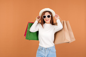 A beautiful Asian woman wearing a white long sleeve sweater and jeans, carrying a paper bag with items bought from a department store.