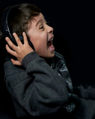 Happy little boy listening to music on headphones and shouting, black background