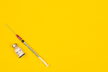 Bottle of Covid-19 coronavirus vaccine and syringe put on yellow background with copy space. Concept for spreading of a cure for virus outbreak