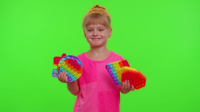Stylish child girl dancing and holding many colorful squishy silicone bubbles sensory toy. Kid playing push pop it popular educational children game. Trend 2021. Chroma key green screen. Stress relief